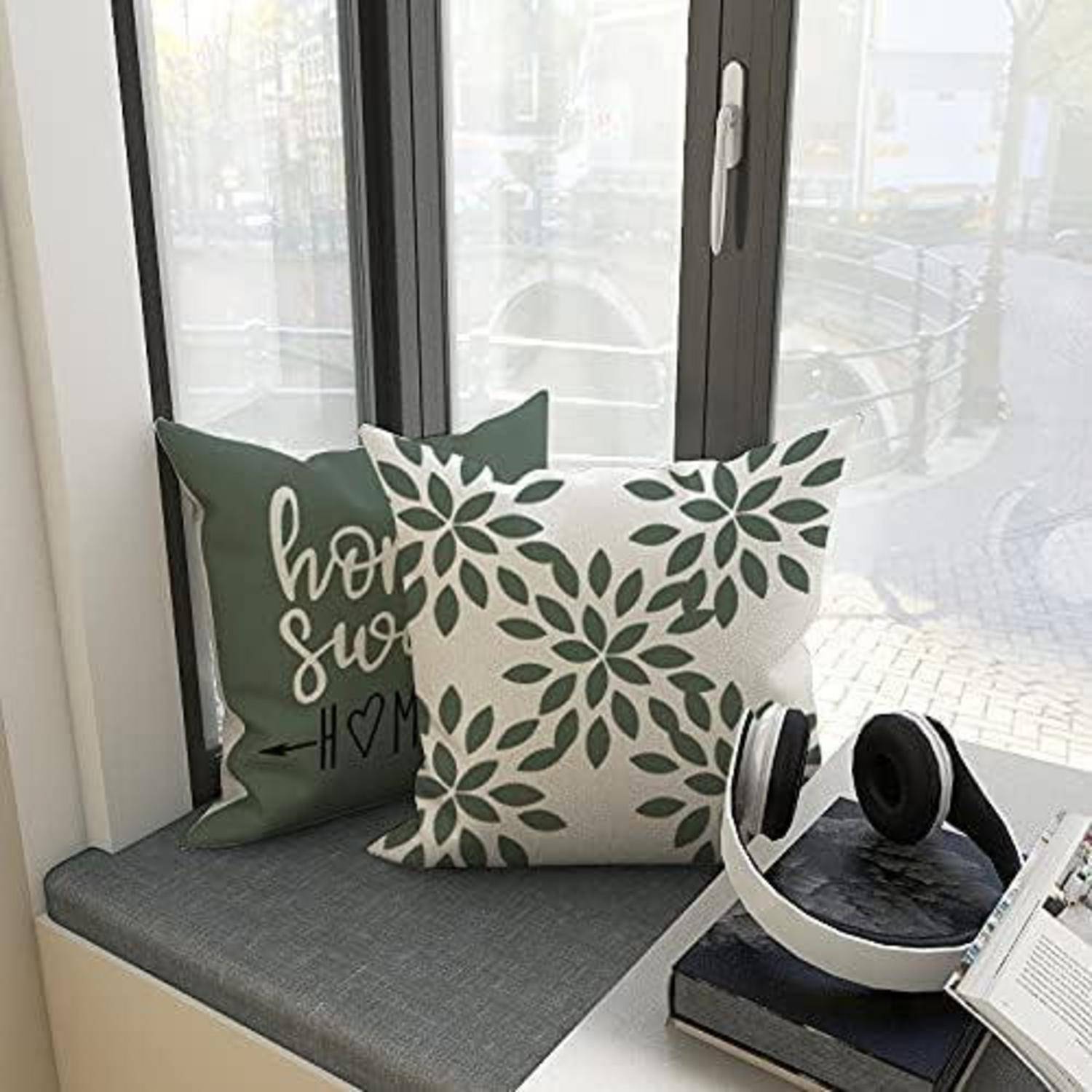 Ein Fensterplatz mit zwei dekorativen Kissen und einem Kopfhörerpaar. Ein Kissen hat ein Blattmuster, das andere trägt die Aufschrift „Zuhause, süßes Zuhause