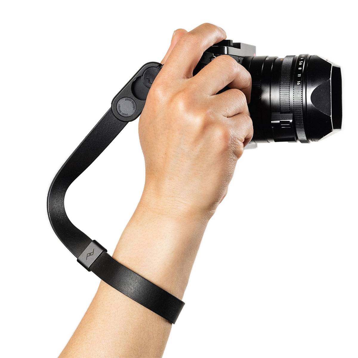 Eine Hand hält eine Digitalkamera mit einem schwarzen Trageriemen zur Stabilität und demonstriert einen festen Griff.