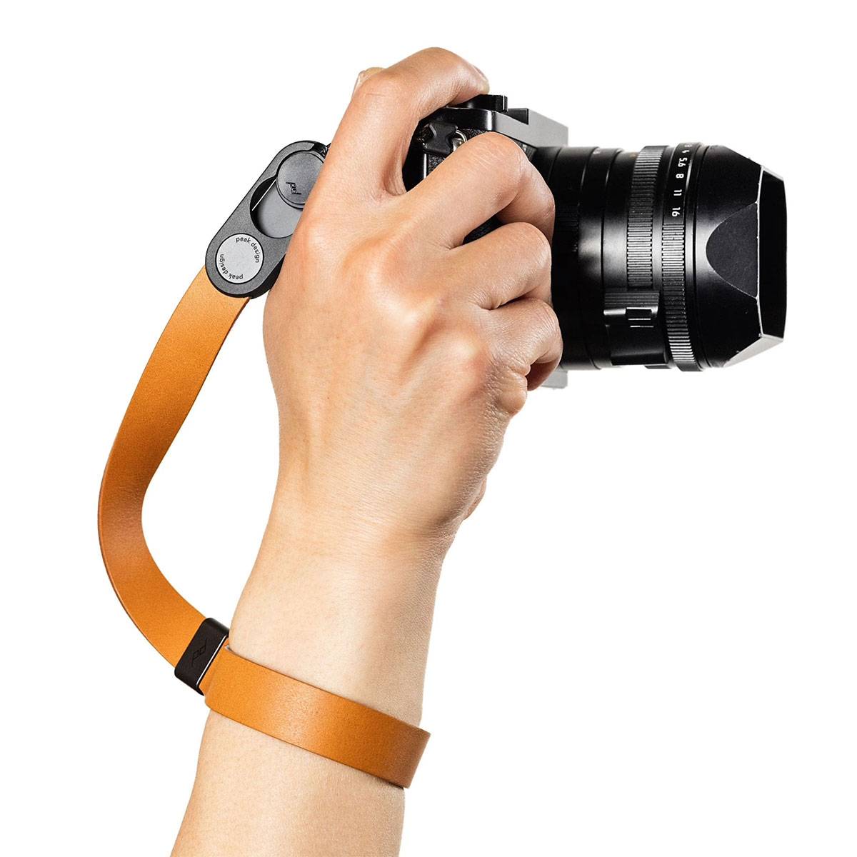 Eine Hand, die eine Kamera mit einem braunen Handgelenkband hält und in Position ist, um ein Foto zu machen. Das Objektiv ist groß und prominent in Szene gesetzt.