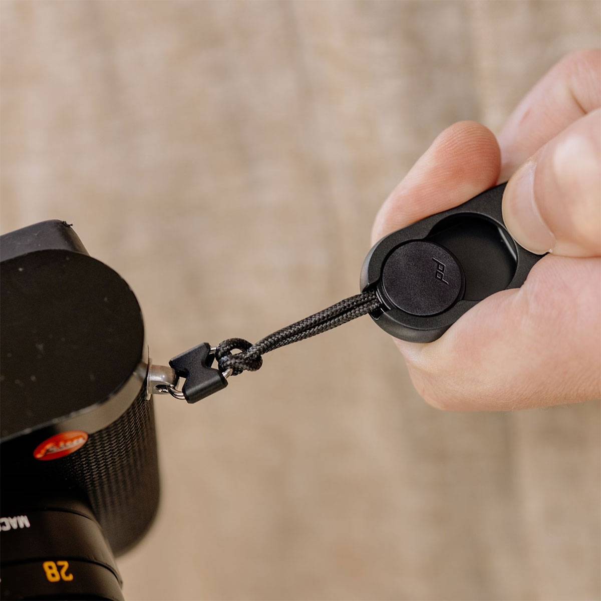 Eine Person befestigt eine Objektivkappe an einer Kamera mit einem Handgelenkband.