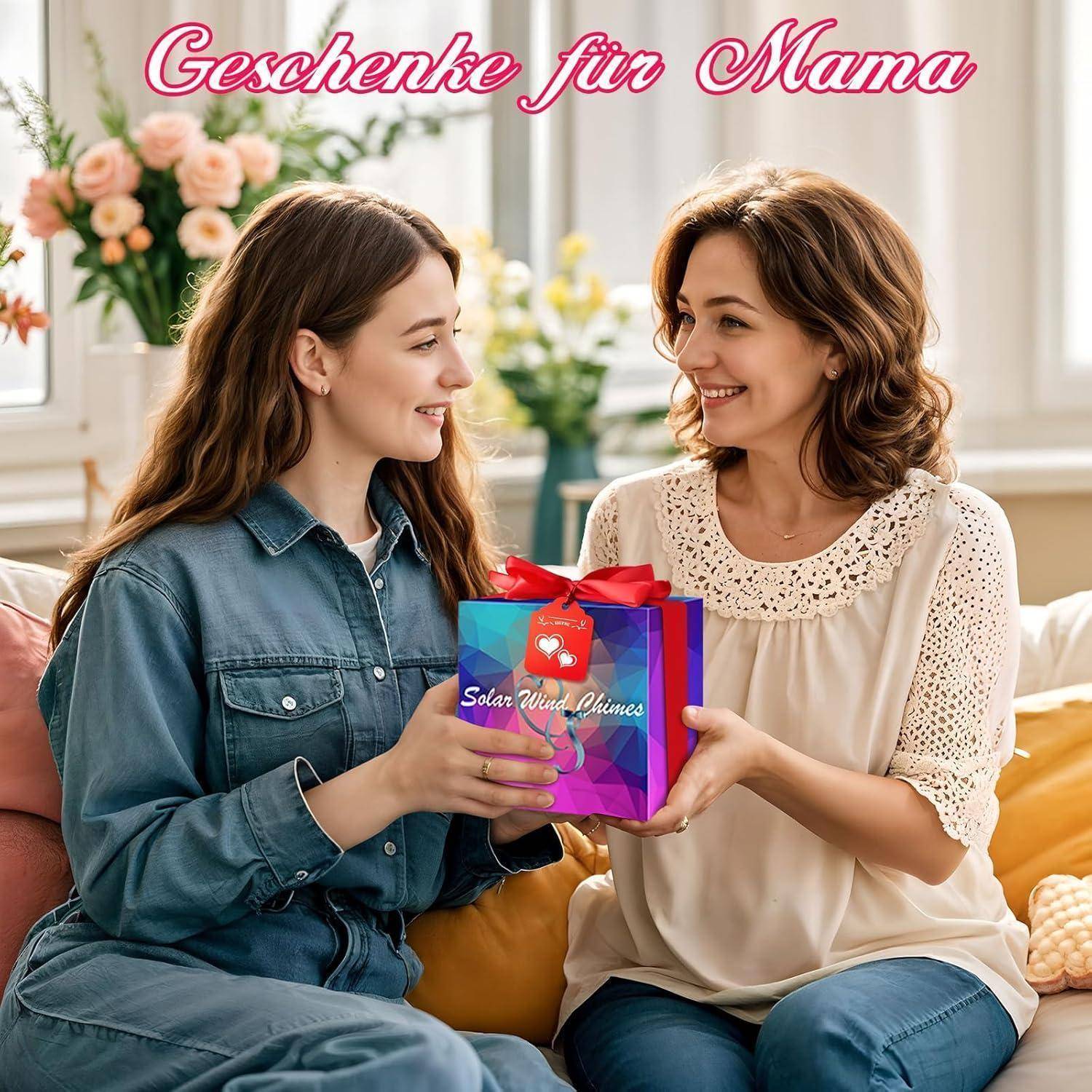 Zwei Frauen lächeln und sitzen auf einem Sofa; die Jüngere reicht der Älteren ein Geschenk. Text oben steht: 'Geschenke für Mama' (Geschenke für Mama).