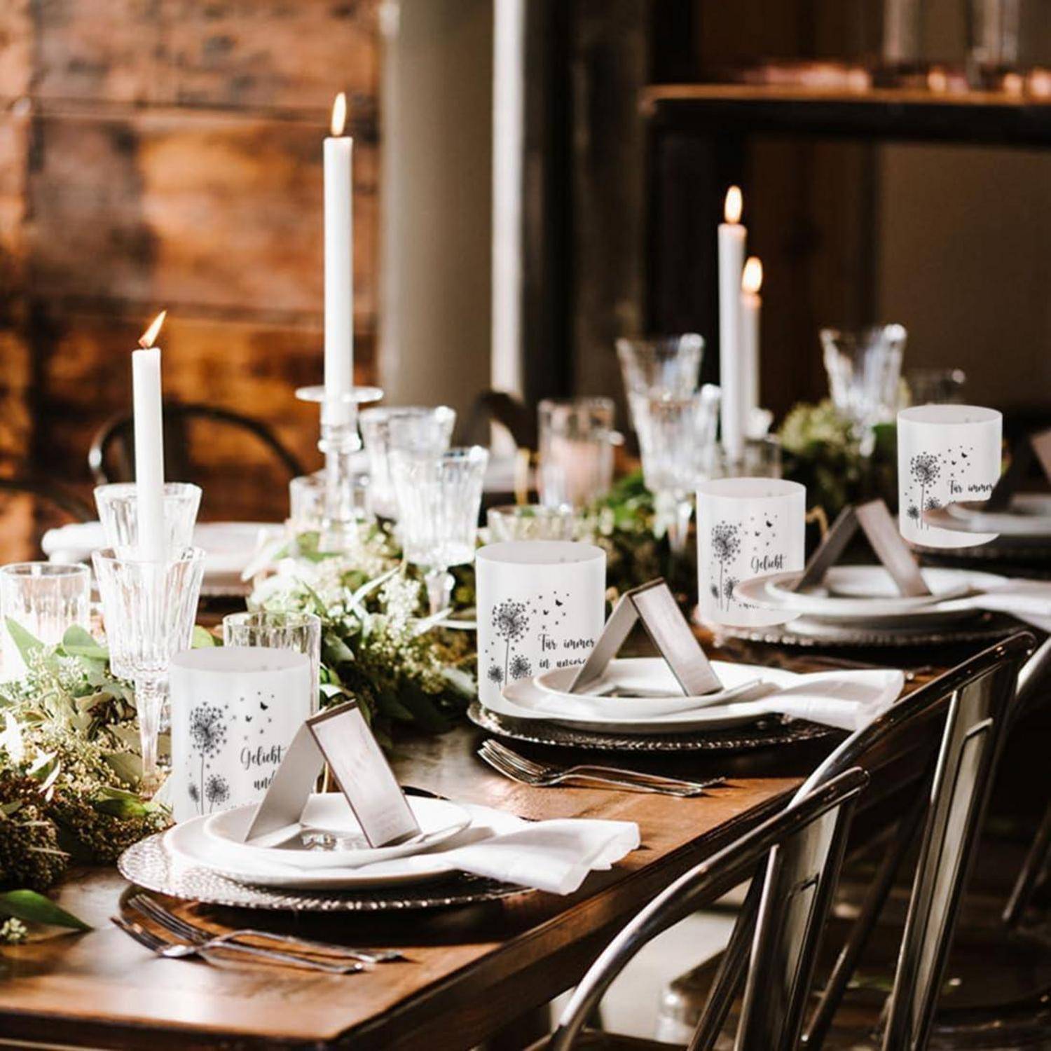 Ein rustikaler, elegant gedeckter Esstisch mit weißen Kerzen, Blumenarrangements und dekorierten Tellern, der eine warme und einladende Atmosphäre schafft.