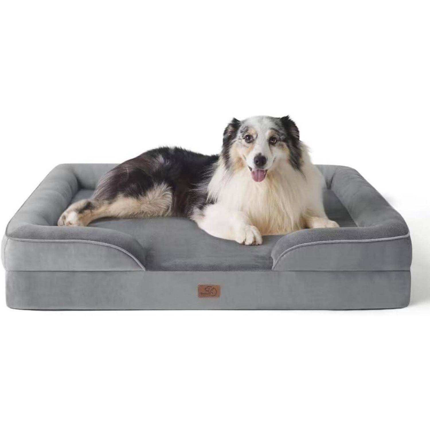 Ein Hund mit einem weiß-schwarzen Fell liegt behaglich auf einem großen, grauen, gepolsterten Tierbett und wirkt zufrieden und entspannt.