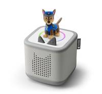 Ein kleiner grauer Lautsprecher mit einer Hundefigur in blauer Uniform oben drauf, der einem Kinderspielzeug ähnelt. Die Audiobuchsen bilden eine Silhouette eines Katzenkopfes.