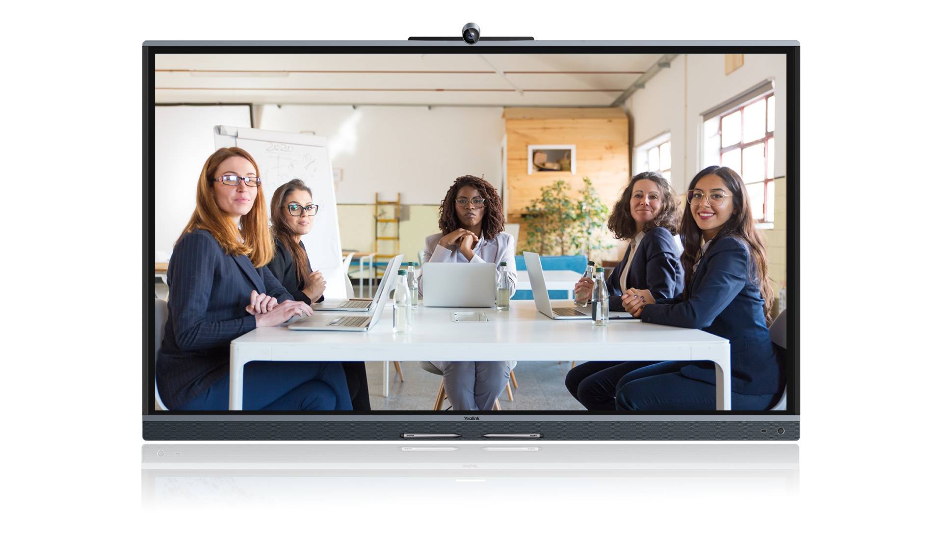 Videokonferenz auf einem großen Monitor, die fünf Frauen zeigt, die um einen Tisch in einem hellen Büro sitzen, jede mit einem Laptop.