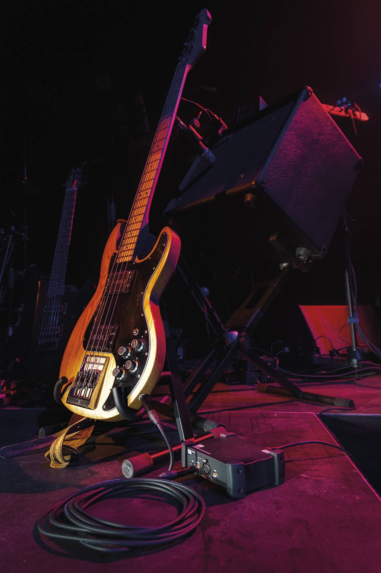 Eine E-Gitarre ruht auf einem Ständer neben der Bühnentontechnik, von Bühnenlichtern gedämpft beleuchtet, bereit für einen Live-Auftritt.