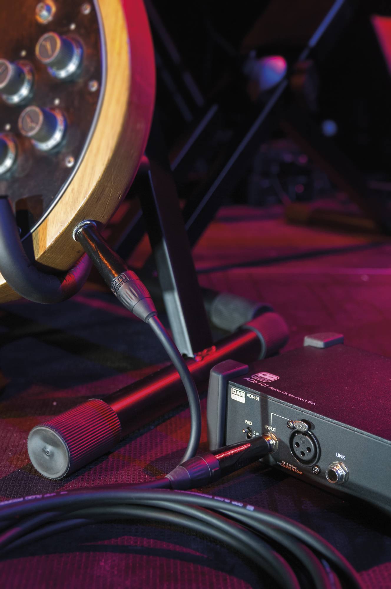 Eine Gitarre ist über ein Audiointerface-Gerät auf einer Bühne angeschlossen, wobei Kabel und Ausrüstung im Hintergrund sichtbar sind.