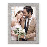 Ein Paar, förmlich gekleidet, mit der Frau, die einen Blumenstrauß hält, umarmen sich liebevoll im Freien auf einem gerahmten Foto.