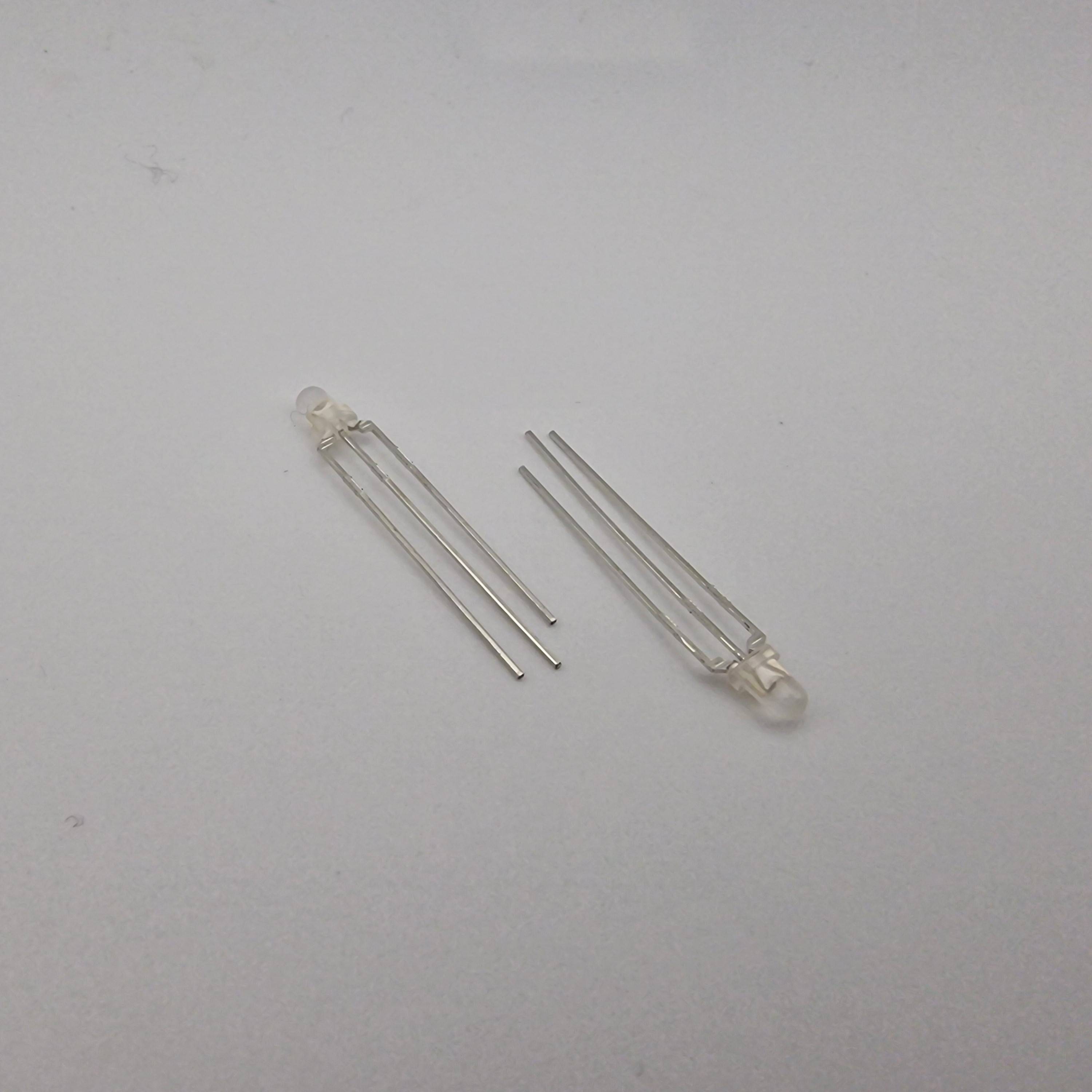 Zwei transparente Leuchtdioden (LEDs) mit Metallstiften auf einer weißen Oberfläche, parallel und leicht voneinander entfernt positioniert.