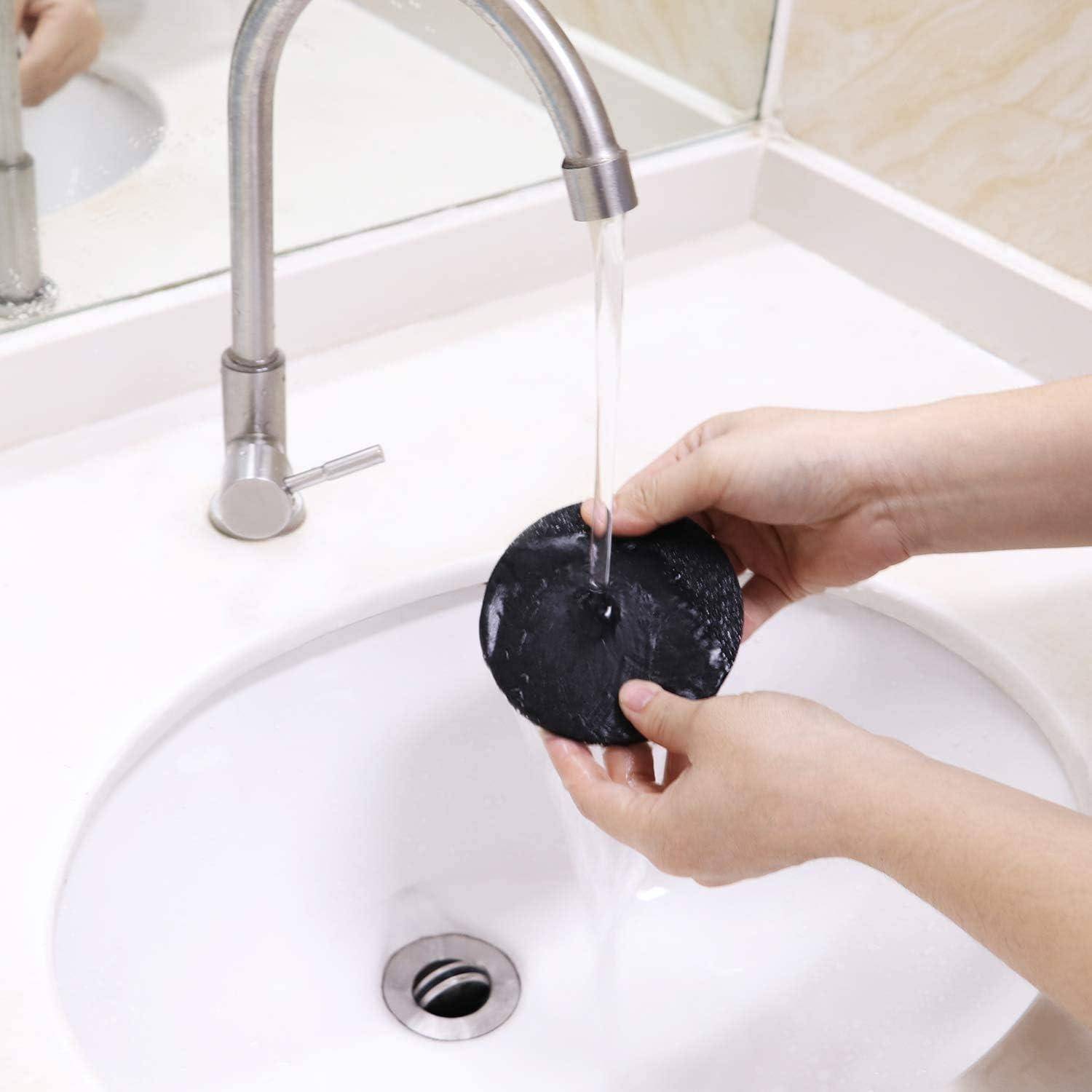 Eine Person wäscht ein rundes schwarzes Objekt unter einem Wasserstrahl aus einem modernen Wasserhahn in einem weißen Waschbecken.