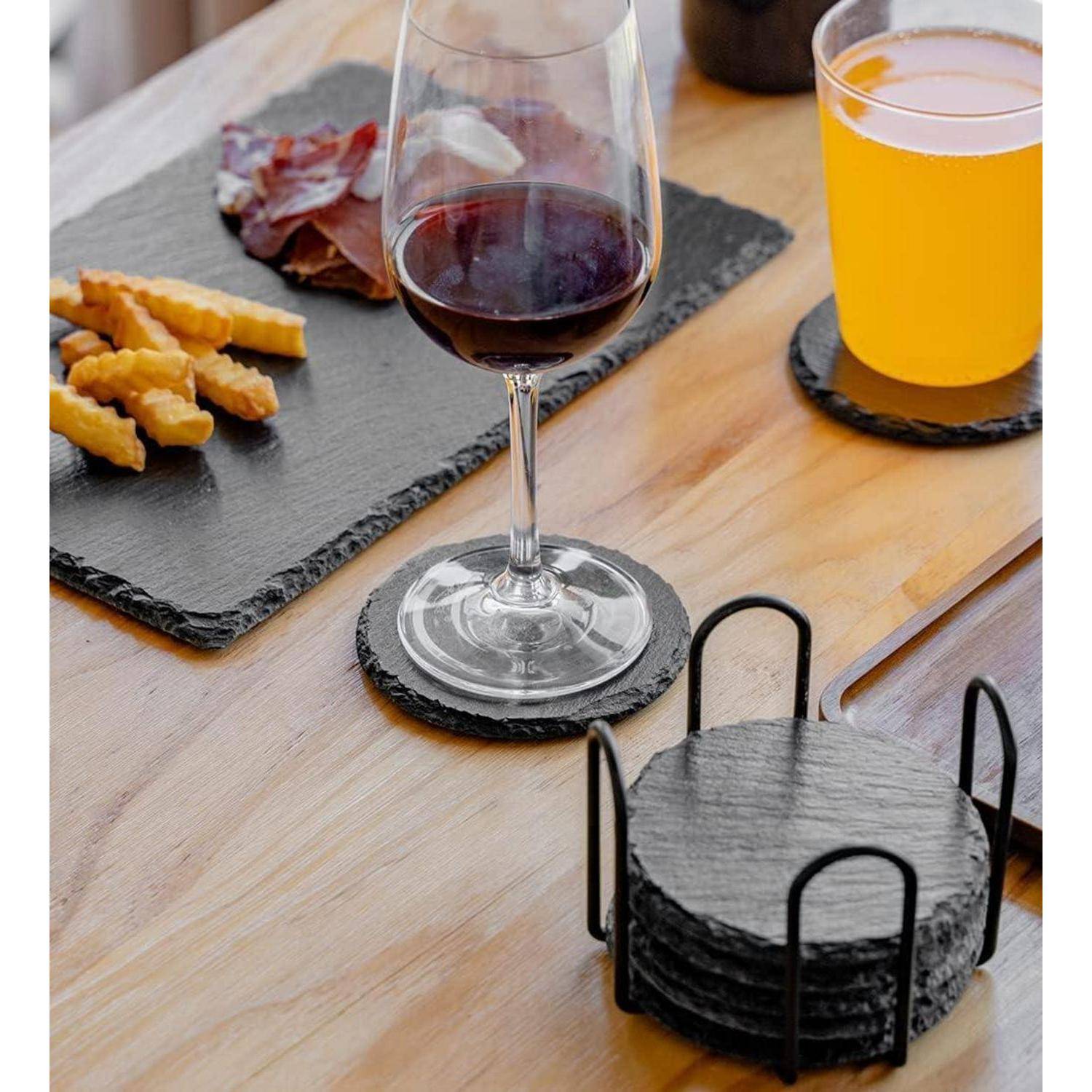 Ein Glas Rotwein und ein Glas Orangensaft stehen auf einem Tisch mit einer Schieferplatte, Käse, Aufschnitt und runden Untersettern.