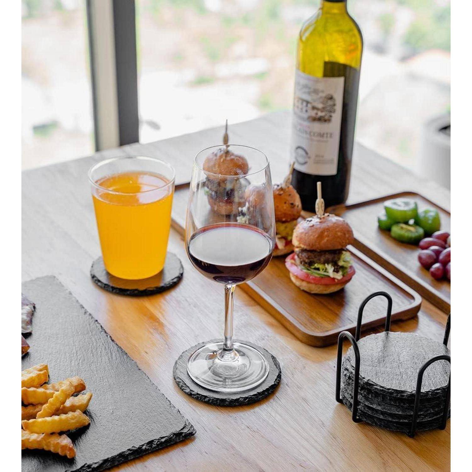 Ein gedeckter Tisch mit einem Glas Orangensaft, einem Glas Rotwein, Mini-Burgern, Pommes, Trauben, geschnittenen Paprikaschoten und einer Weinflasche.