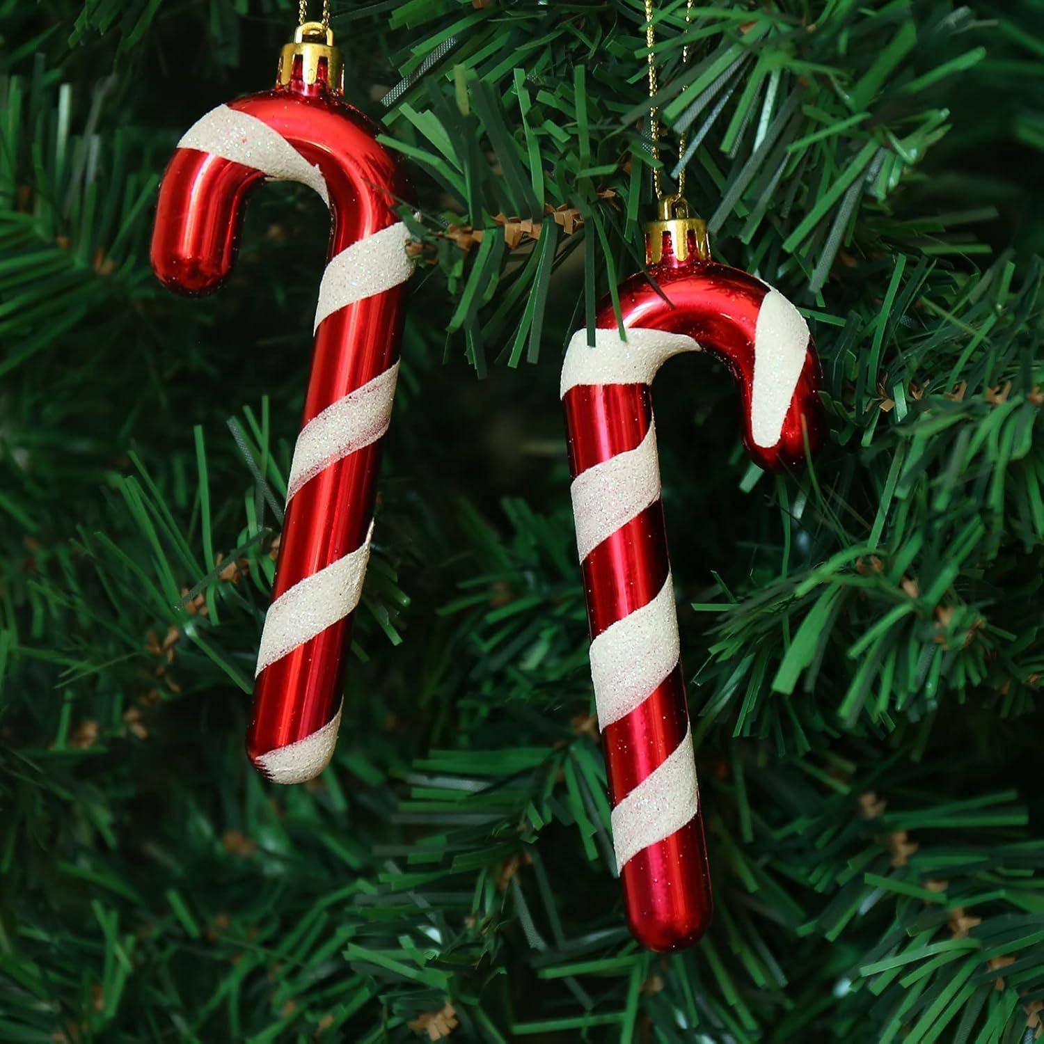 Zwei rot-weiße Zuckerstangenornamente hängen an einem grünen Weihnachtsbaumast.
