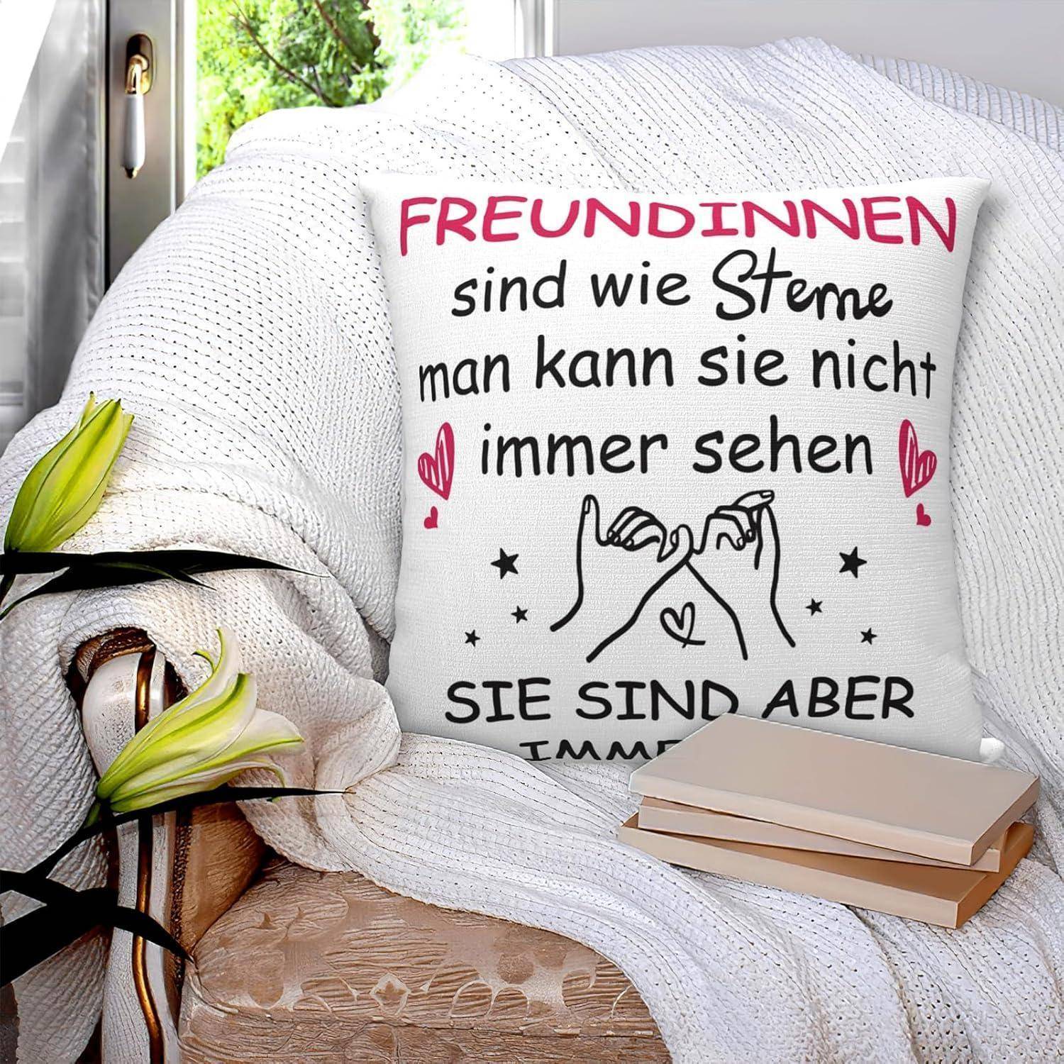 Ein Kissen auf einem Stuhl zeigt deutschen Text über Freundschaft, umgeben von Herz- und Handzeichnungen. Ein Fenster und Bücher befinden sich in der Nähe.