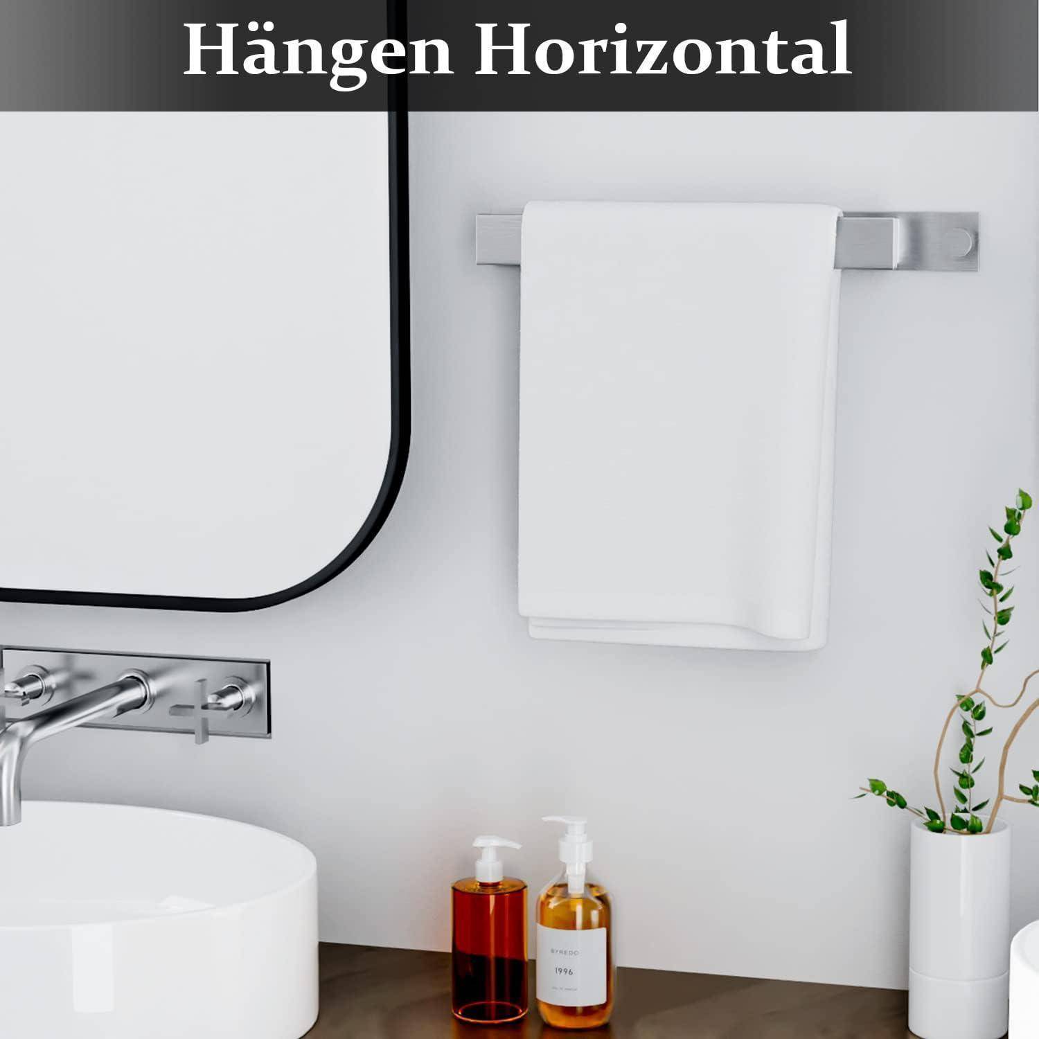 Ein modernes Badezimmer mit einem runden Spiegel, einem Handtuch an der Stange, einem weißen Waschbecken, zwei Seifenspendern und einer Pflanze daneben vor einer weißen Wand.