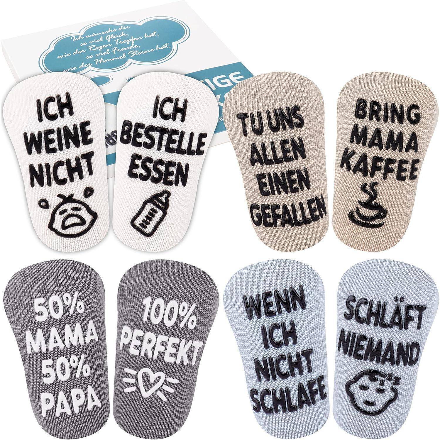 Socken mit deutschen Phrasen: 'Ich weine nicht', 'Ich bestelle Essen', 'Bring Mama Kaffee', '50% Mama', '50% Papa', '100% perfekt', 'Wenn ich nicht schlafe, schläft niemand'.