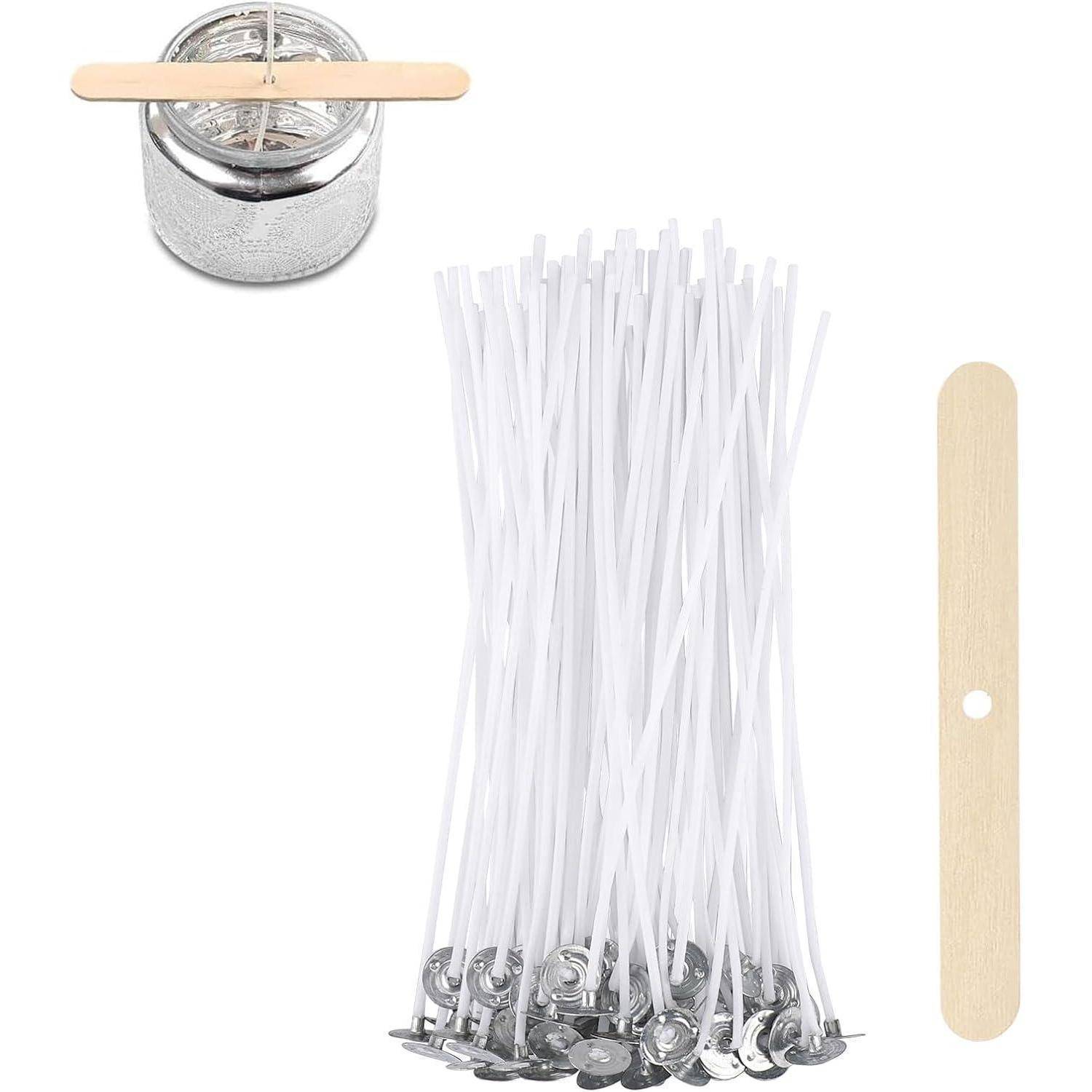 Ein Bündel weißer Kerzendochte mit Metallbasen neben einem kleinen Metallbehälter und einem Holzstab mit einem zentralen Loch, der zum Herstellen von Kerzen verwendet wird.