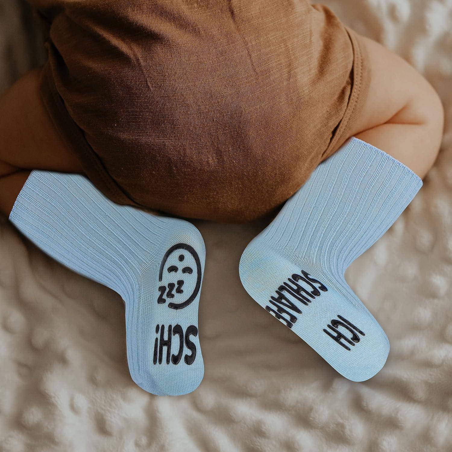 Ein Baby trägt hellblaue Socken mit verspieltem Text und einem Smiley-Gesicht und liegt auf einer weichen, strukturierten Oberfläche. Der Fokus liegt auf den Füßen.