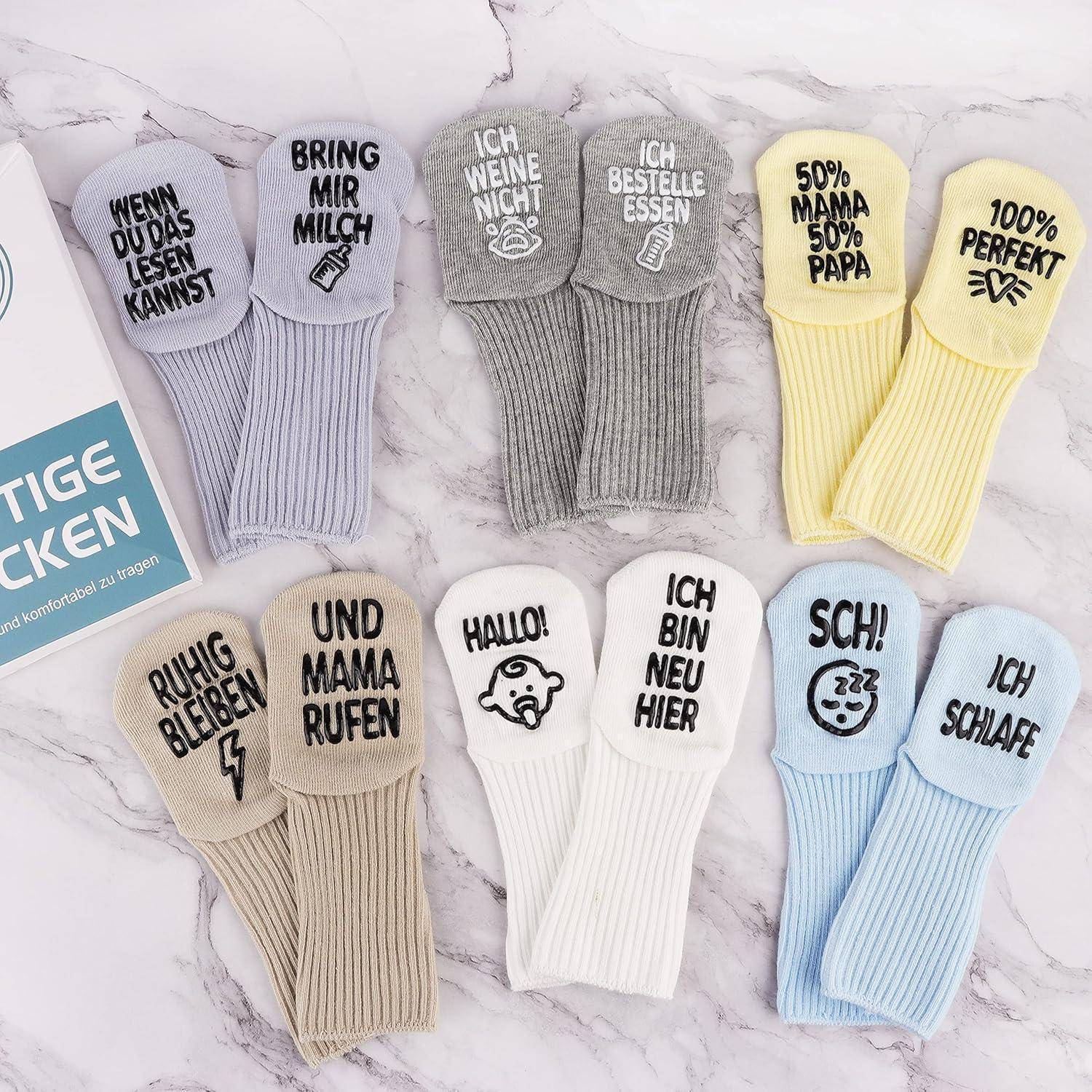 Verschiedene Babysockenpaare mit humorvollen deutschen Phrasen, wie zum Beispiel "Wenn du das lesen kannst, bring mir Milch"" und ""Ich weine nicht, ich bestelle Essen."