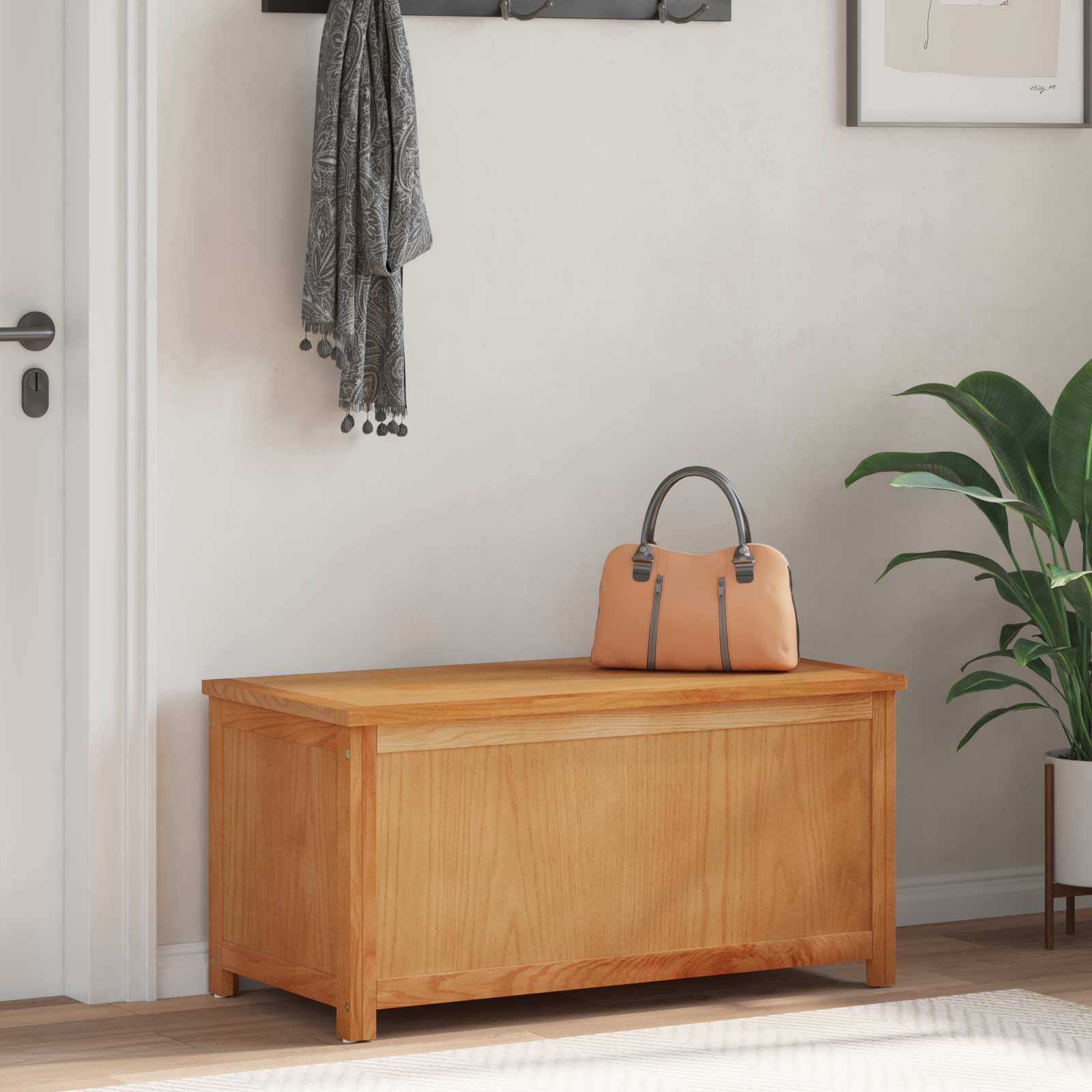 Eine Holzbank mit einer Ledertasche darauf steht in einem Flur, in dem ein grauer Schal in der Nähe hängt und eine Pflanze in der Ecke steht.