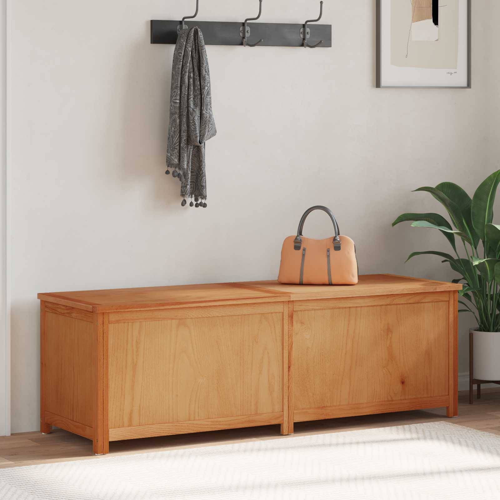 Eine Holzaufbewahrungsbank steht an einer Wand mit einer Garderobe darüber, an der ein Schal und eine Tasche hängen. Eine Topfpflanze steht in der Nähe.