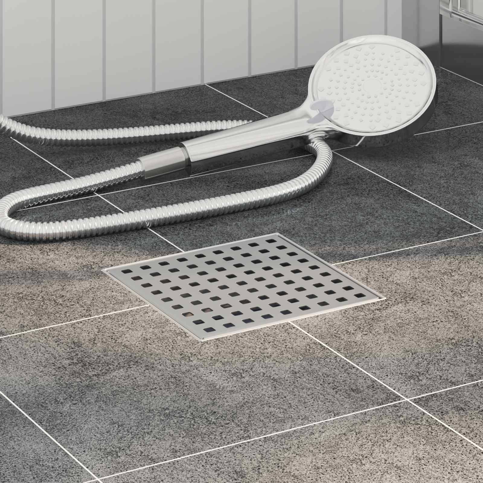 Eine Handbrause mit Kabel liegt auf einem grauen gefliesten Badezimmerboden neben einem quadratischen Abfluss, was eine moderne Badezimmereinrichtung veranschaulicht.