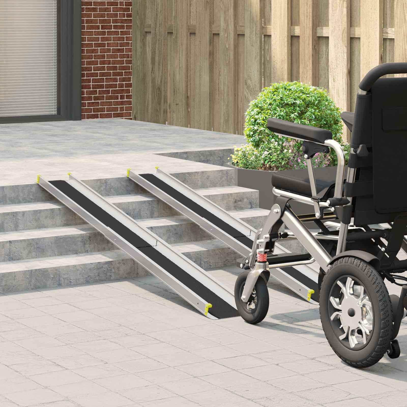 Ein Elektrorollstuhl steht neben einer tragbaren Rampe, die zu einigen Stufen hinauf zu einer Terrasse führt, was auf Barrierefreiheit für Rollstuhlfahrer hindeutet.