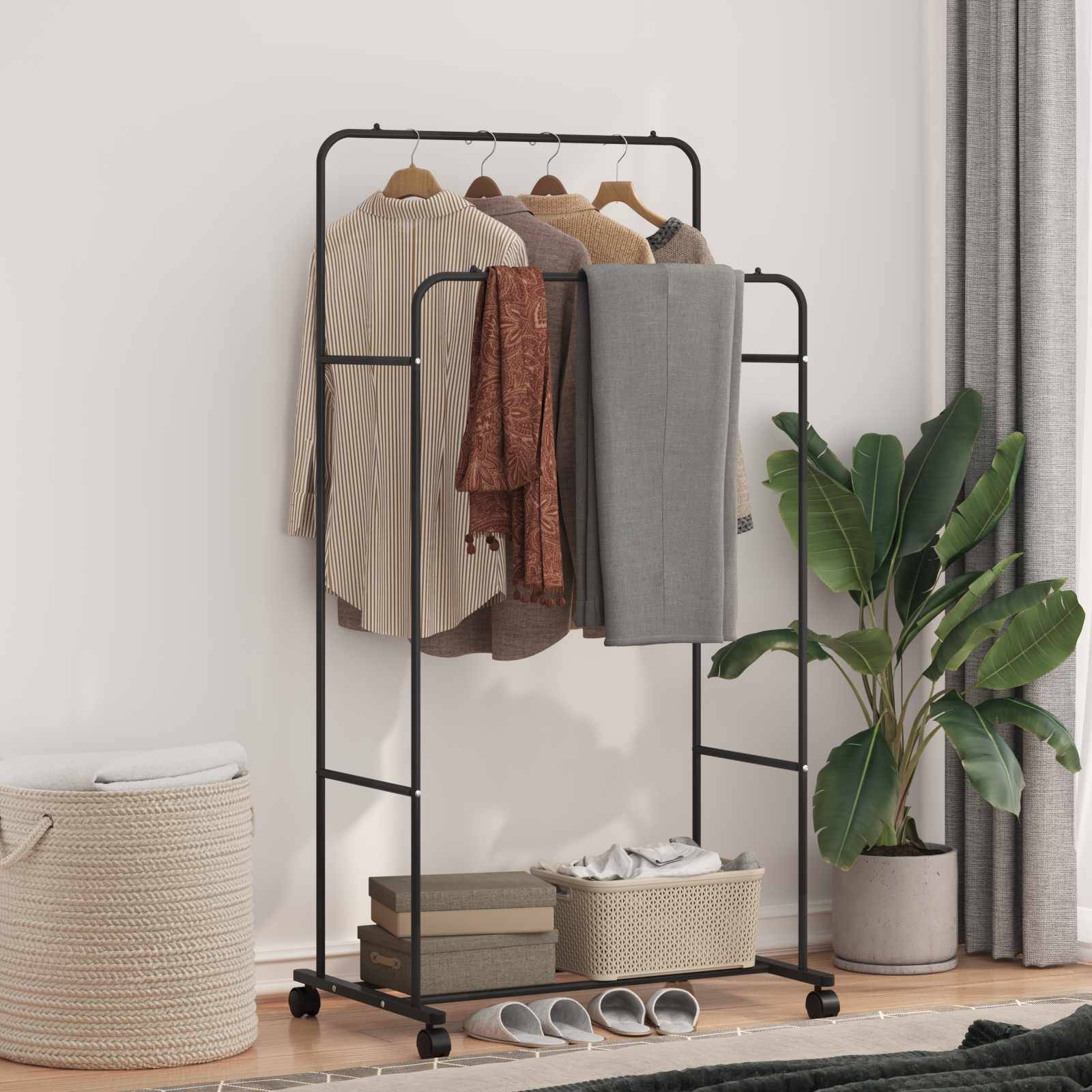 Eine schwarze Metallkleiderstange hält mehrere Kleidungsstücke, darunter einen Mantel, eine Jacke und eine Hose. Eine große Pflanze steht daneben.