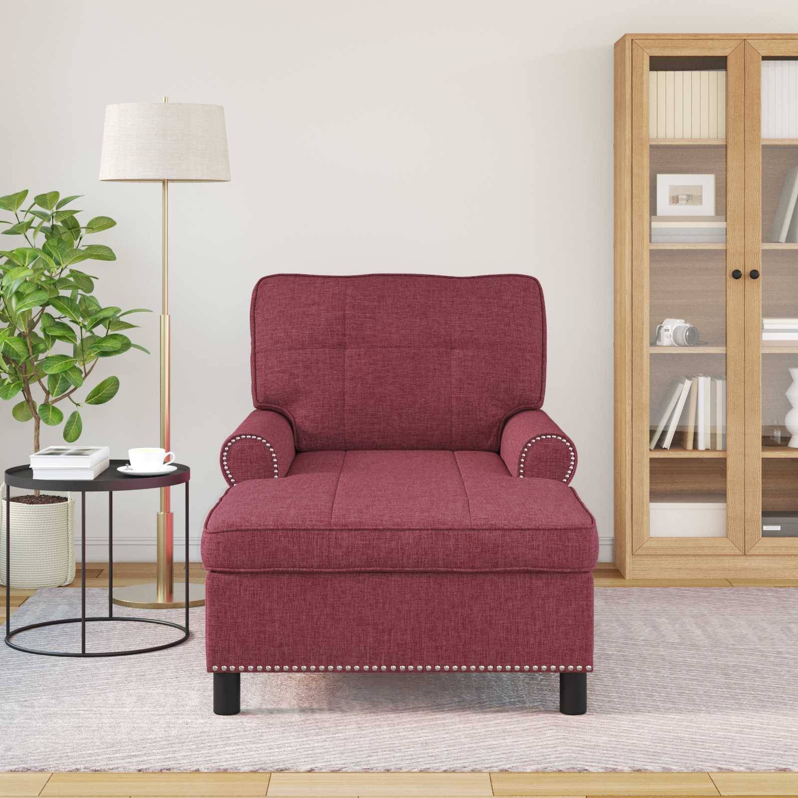 Ein roter Sessel mit Ziernieten ist mittig auf einem Teppich platziert. Links davon ein kleiner Tisch mit einer Tasse und einer Pflanze; rechts ein Schrank mit Büchern.