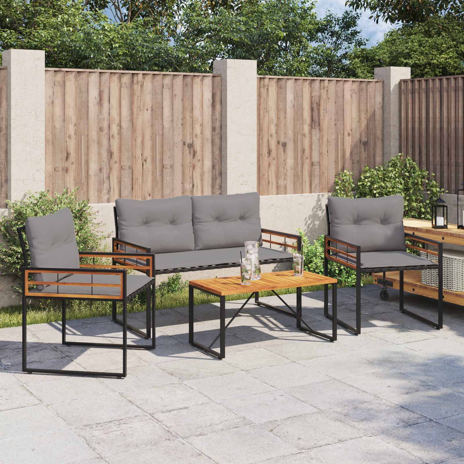 Outdoor-Gartenmöbel-Set mit einem Holztisch und zwei grauen gepolsterten Stühlen sowie einer Sitzbank auf einer gepflasterten Fläche, umgeben von einem Holzzaun.
