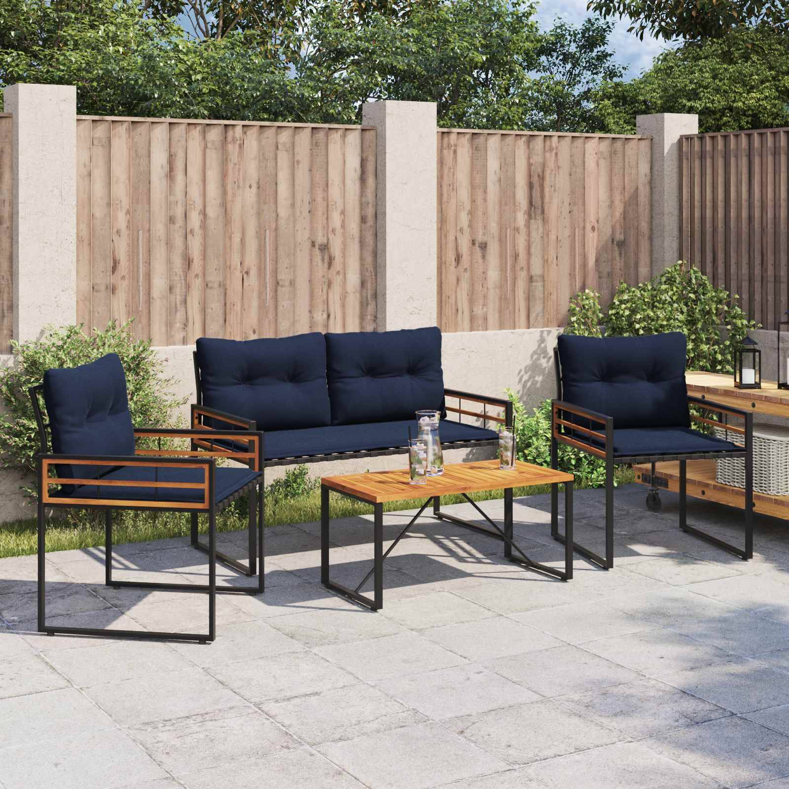 Außenbereich mit Terrasse, ausgestattet mit zwei marineblau gepolsterten Stühlen, einer Sitzbank und einem Tisch auf einem gefliesten Boden. Im Hintergrund ein Holzzaun und Grünpflanzen.
