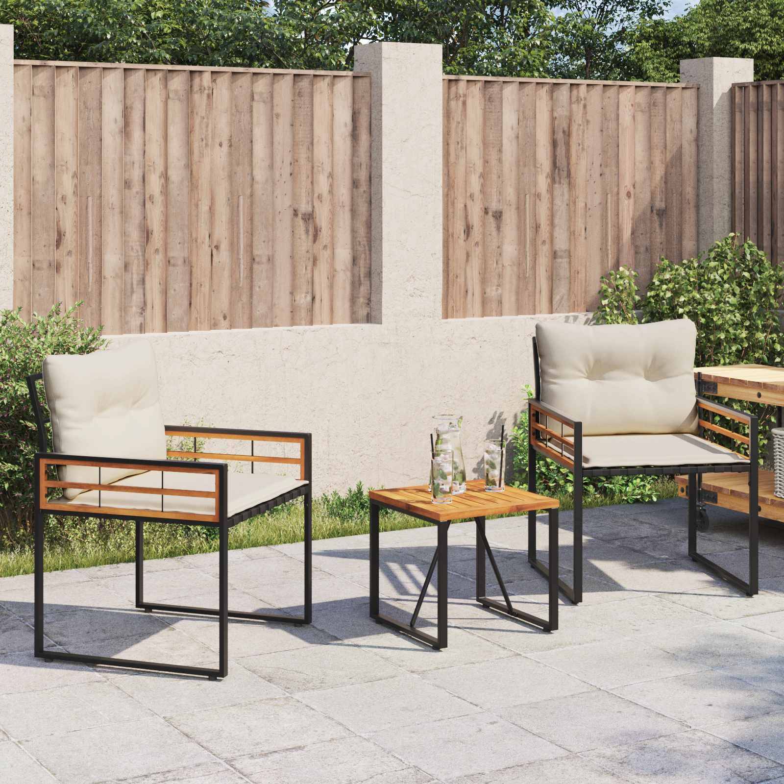 Patio mit zwei gepolsterten Stühlen und einem kleinen Holztisch auf einer gefliesten Oberfläche, angrenzend an einen Holz- und Betonnzaun, umgeben von Grünpflanzen.
