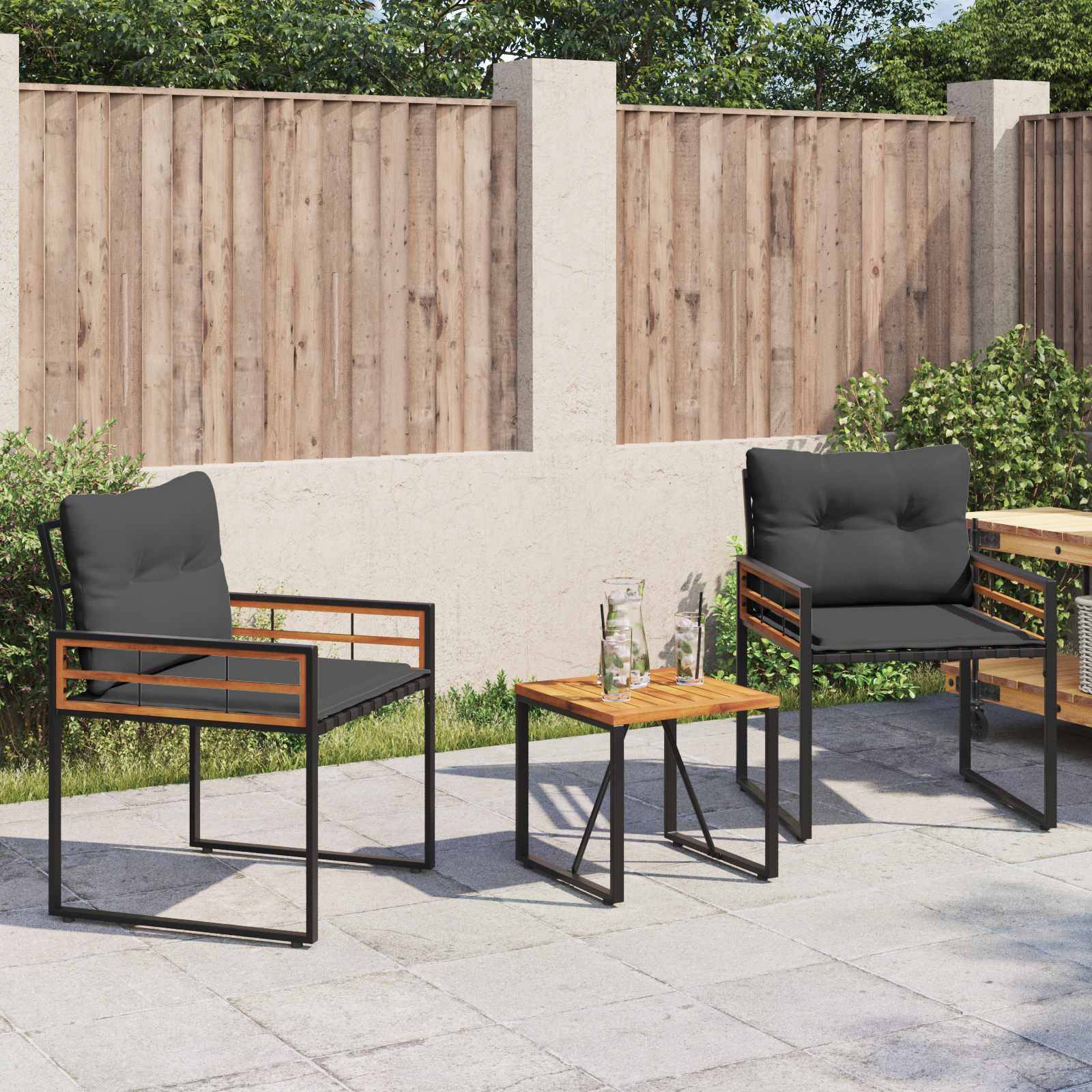 Eine Terrasse mit zwei schwarzen gepolsterten Stühlen und einem kleinen Holztisch, auf dem zwei Gläser stehen, vor einem Holzzaun als Hintergrund.