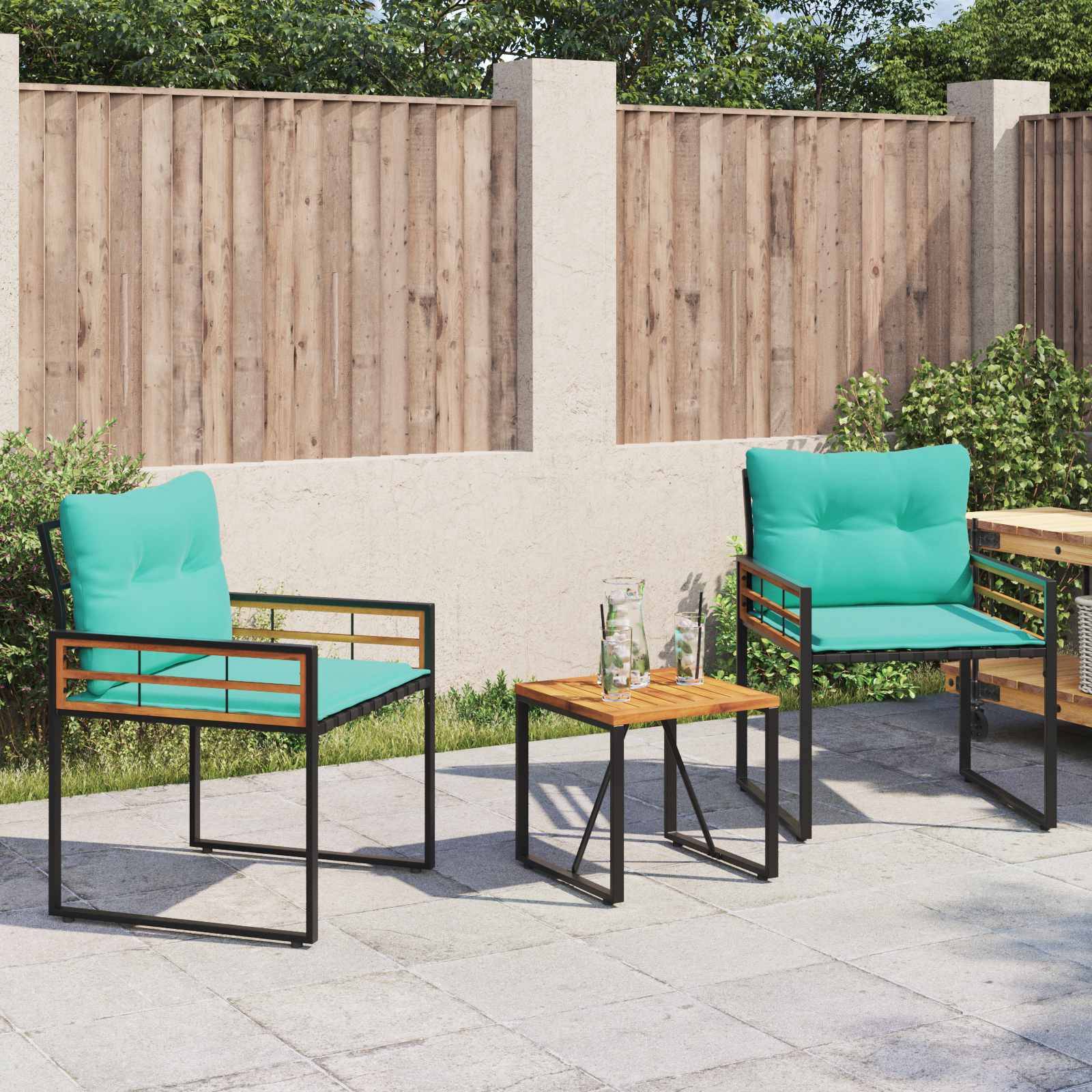 Zwei petrolblaue gepolsterte Stühle und ein kleiner Tisch mit Gläsern stehen auf einer Terrasse, begrenzt von einem Holzzaun und Grünpflanzen im Hintergrund.
