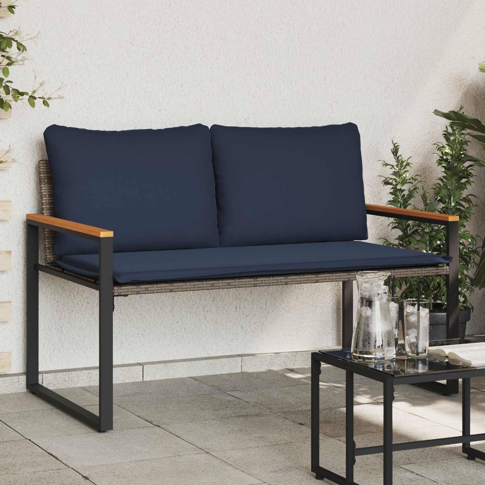 Eine moderne Outdoor-Terrasse mit einer dunkelblau gepolsterten Bank, einem kleinen Glastisch mit Glaswasserkrügen und grünen Pflanzen in der Nähe.