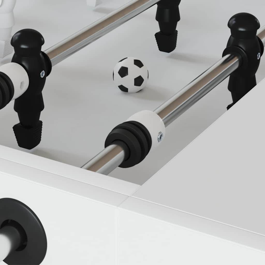 Nahaufnahme eines Kickertischs mit einem Fußball, der mittig auf dem Spielfeld positioniert ist. Schwarze und weiße Spielerstangen sind im Vordergrund sichtbar.