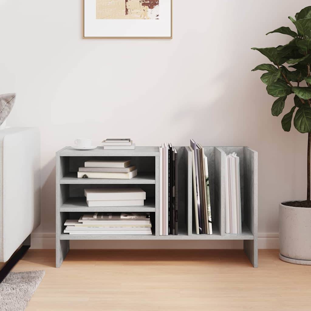 Ein kleines graues Bücherregal hält Bücher und Dokumente ordentlich arrangiert. Rechts daneben steht eine Topfpflanze. Ein Teil eines Sofas ist links sichtbar.
