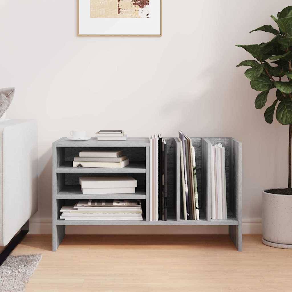 Ein kleines Holzbücherregal neben einem Sofa, gefüllt mit Büchern und Zeitschriften. Eine Topfpflanze steht rechts daneben, und an der Wand hängt Wandkunst.