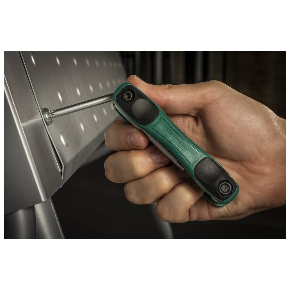 Eine Hand verwendet einen Sechskantschlüssel mit grünem Griff, um eine Schraube auf einer Metalloberfläche anzuziehen.