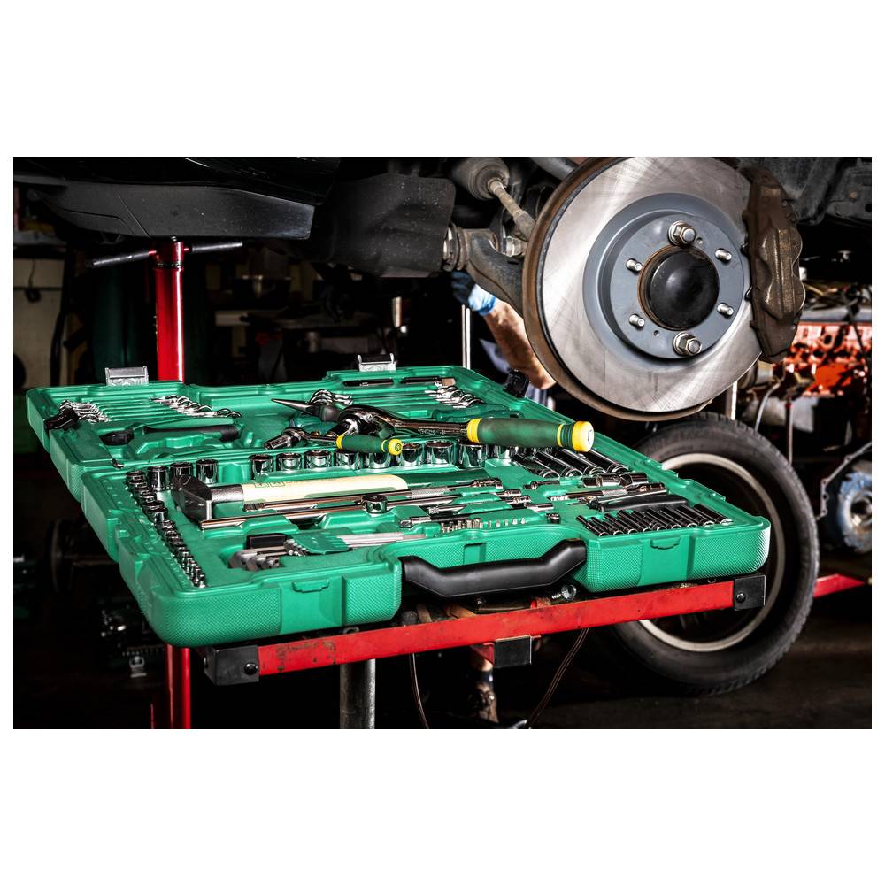 Eine grüne Werkzeugkiste mit verschiedenen Werkzeugen ist in einer Garagenumgebung unter einem Bremssystem eines Autos geöffnet, während dieses gewartet wird.