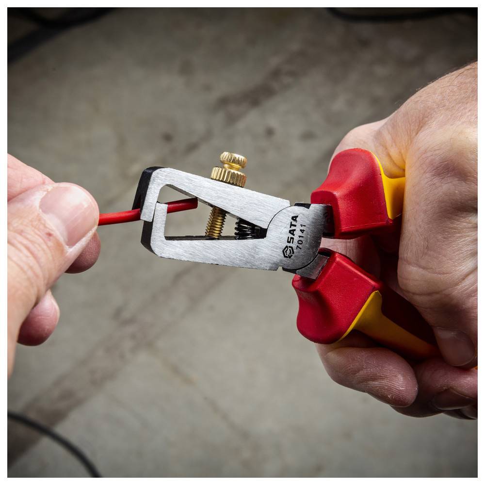 Eine Person verwendet eine Zange mit roten Griffen, um die Isolierung von einem roten Kabel zu entfernen und das Metall darunter freizulegen.