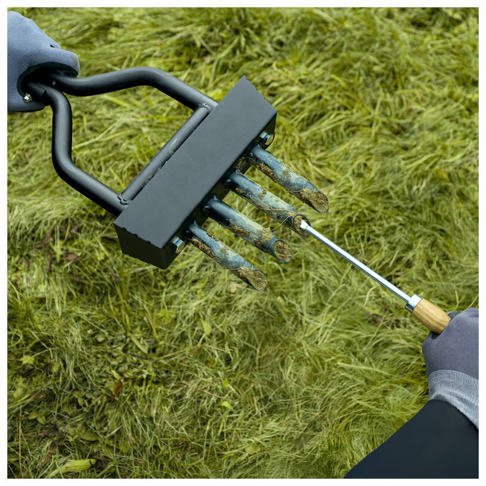 Eine Person verwendet ein Metallinstrument mit einem Griff, um zylindrische Proben aus grasbedecktem Boden zu entnehmen, möglicherweise für Boden- oder Gesundheitsanalysen.