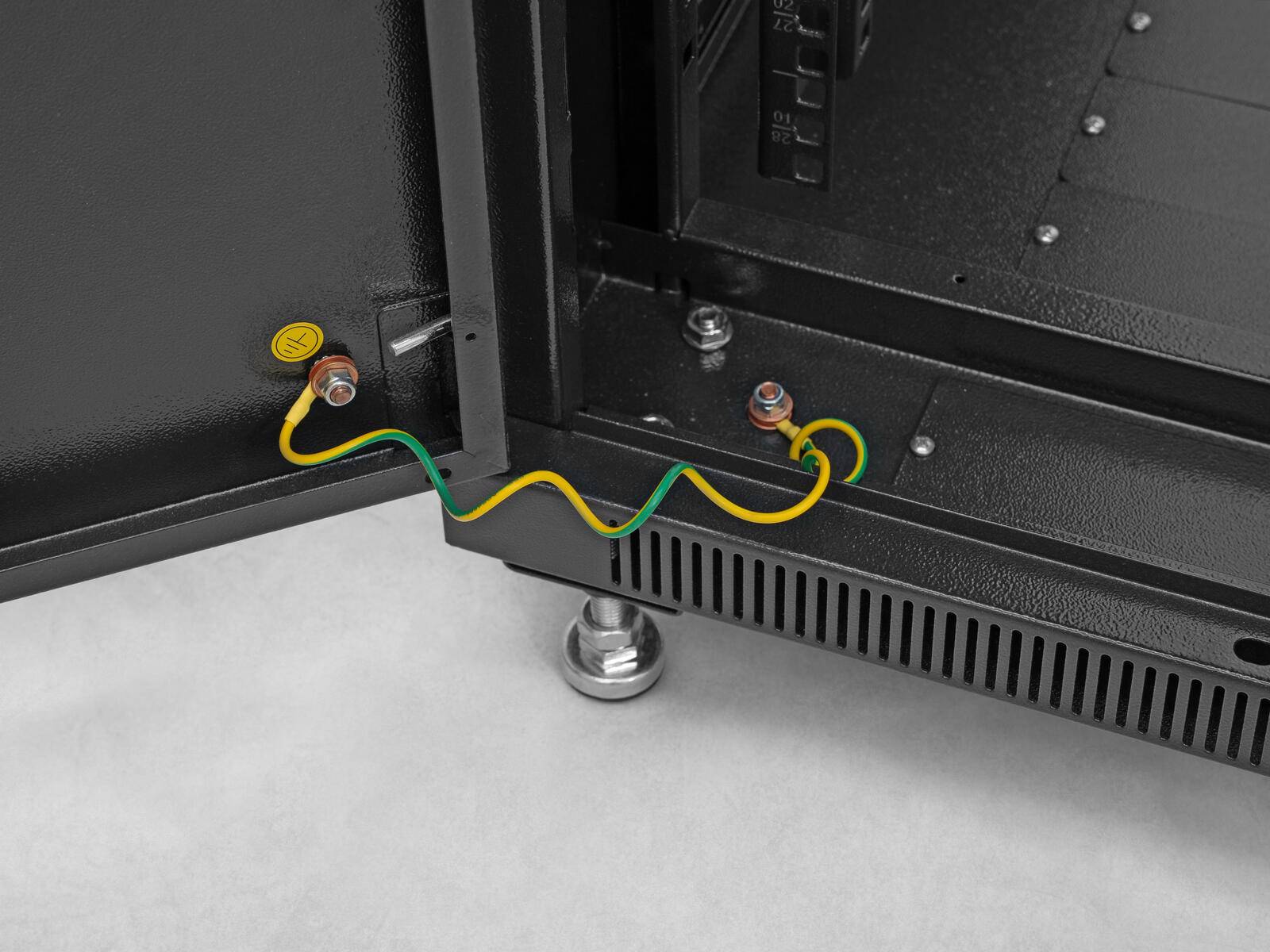 Ein Metallschrank mit einer offenen Tür zeigt einen Erdungsdraht, der an einem Bolzen befestigt ist und damit Maßnahmen zur elektrischen Sicherheit hervorhebt.