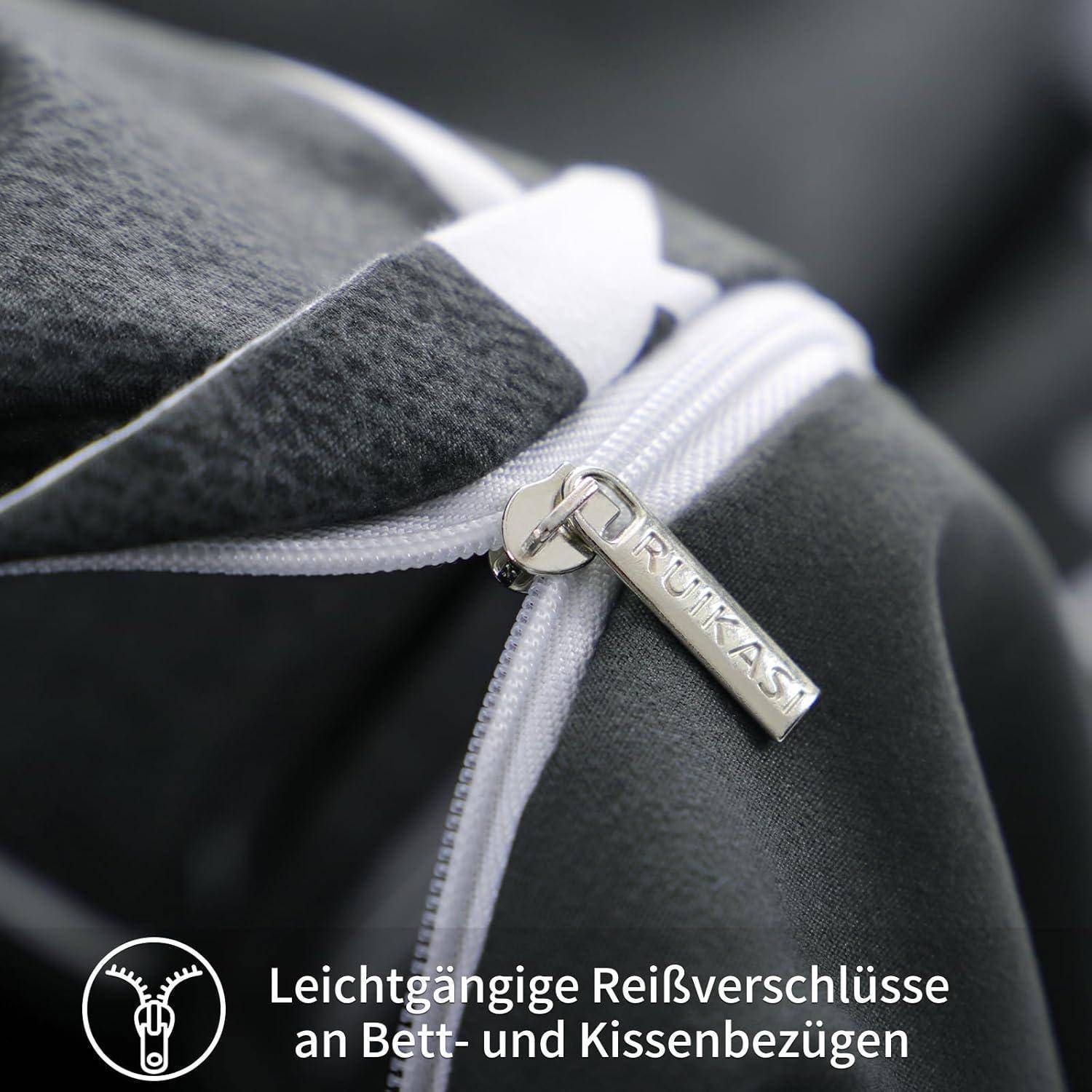 Nahaufnahme eines grauen Stoff-Reißverschlusses mit einem markierten Zuggriff, der einen reibungslosen Mechanismus zeigt. Deutscher Text hebt das einfache Reißverschließen von Bett- und Kissenbezügen hervor.