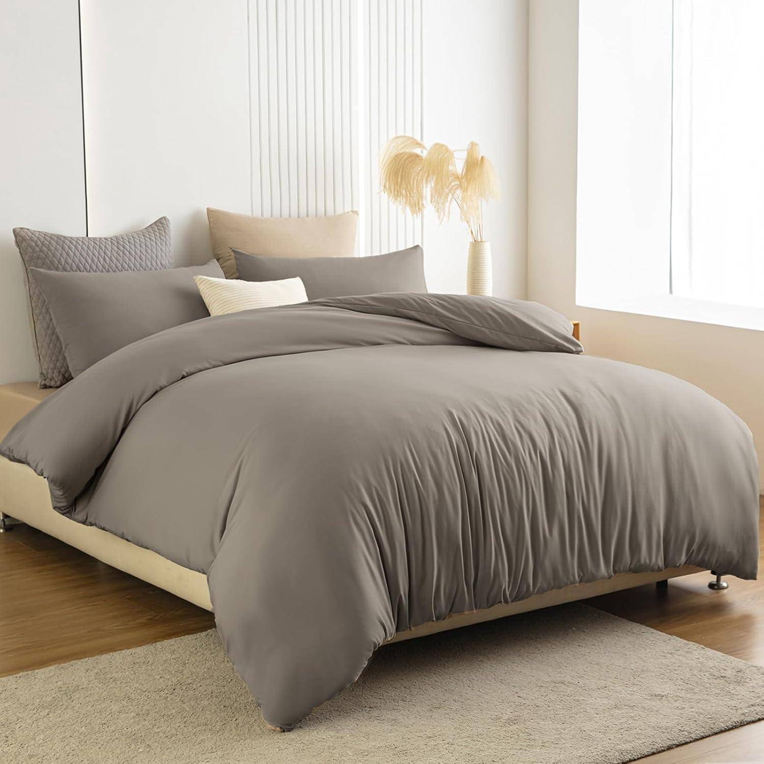 Ein ordentlich gemachtes Bett mit grauer Bettwäsche, Kissen und einer zusammengelegten Decke obenauf. Eine hellbeige Vase mit Pampasgras schmückt den Nachttisch.