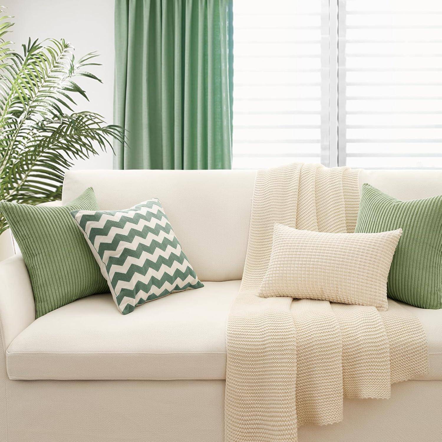 Gemütliches Wohnzimmer mit einem weißen Sofa, grünen Zickzack-gemusterten und einfarbigen Kissen, einer hellen Decke und grünen Vorhängen neben dem Fenster.