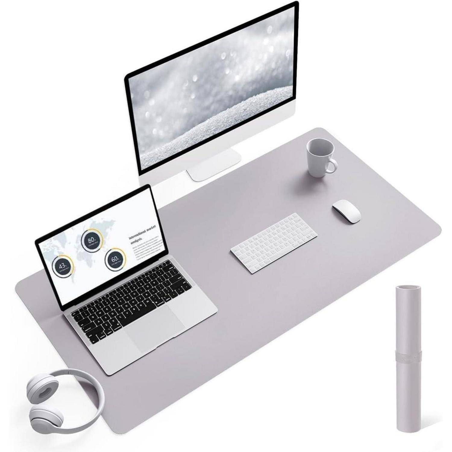 Eine minimalistische Arbeitsplatzeinrichtung mit einem Desktopcomputer, Laptop, Tastatur, Maus, Kopfhörern und einer Kaffeetasse auf einer großen, hellgrauen Unterlage.