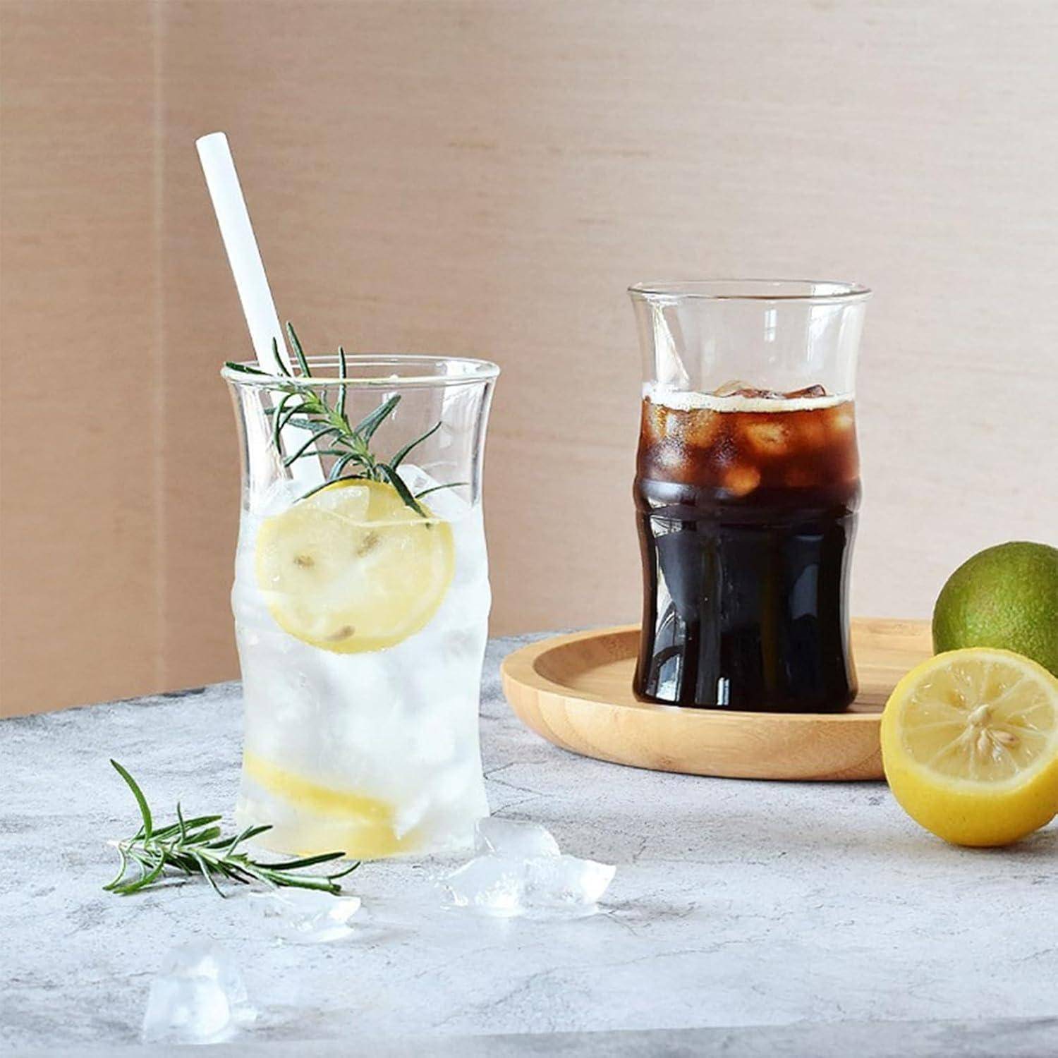 Ein Glas Eiswasser mit Zitrone und Rosmarin neben einem Glas Eiskaffee auf einem Holztablett, mit einer Zitronenhälfte daneben.