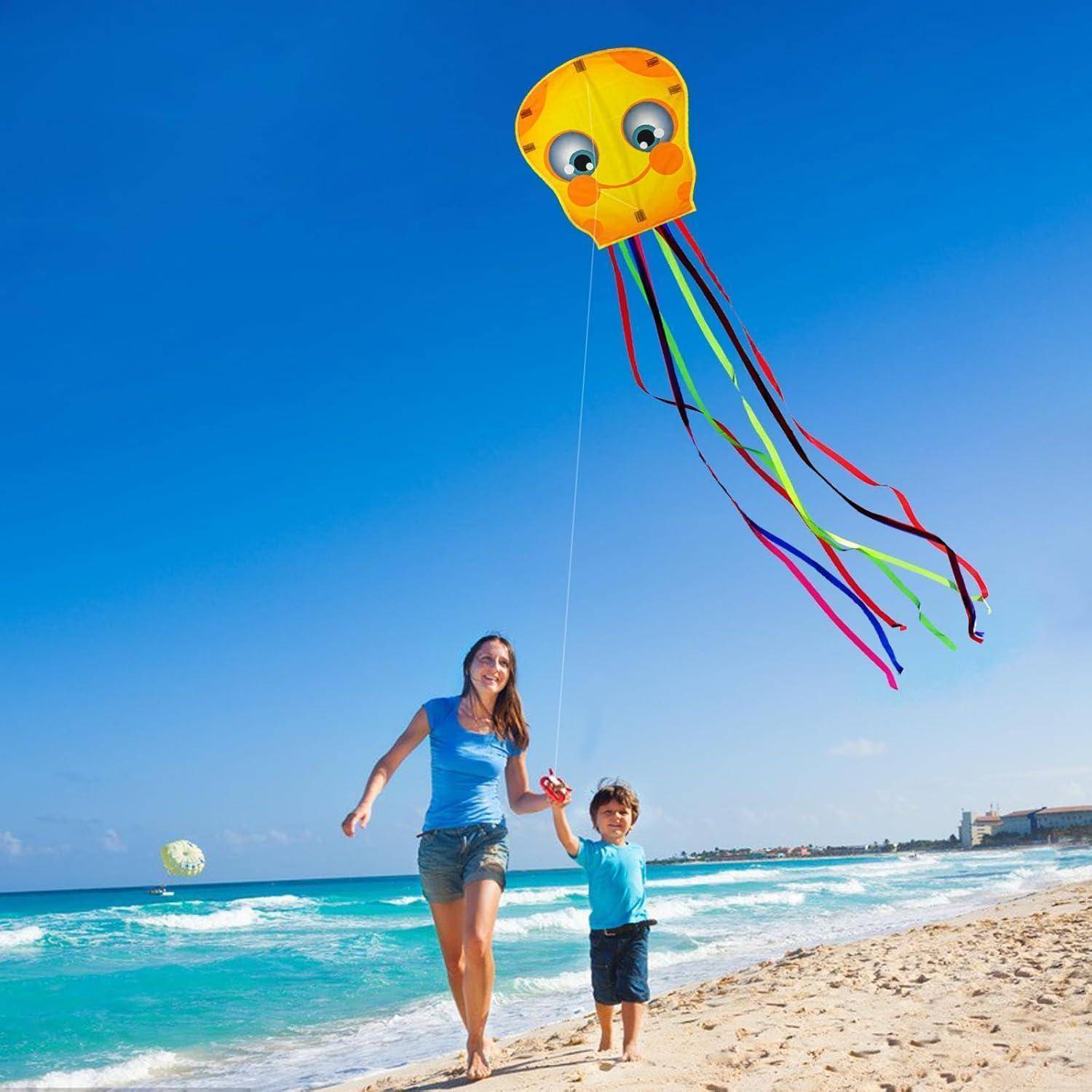 Eine Frau und ein Kind lassen an einem sonnigen Tag an einem sandigen Strand mit dem Ozean im Hintergrund einen bunten, lächelnden Drachen fröhlich in die Luft steigen.