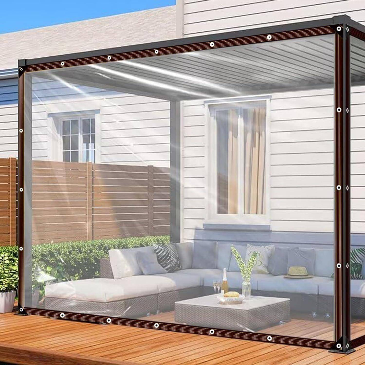 Ein moderner Wintergarten mit transparenten Wänden und einem Metallrahmen, der an ein Haus angebaut ist. Im Inneren befindet sich ein Sofa, ein kleiner Tisch und Kissen.